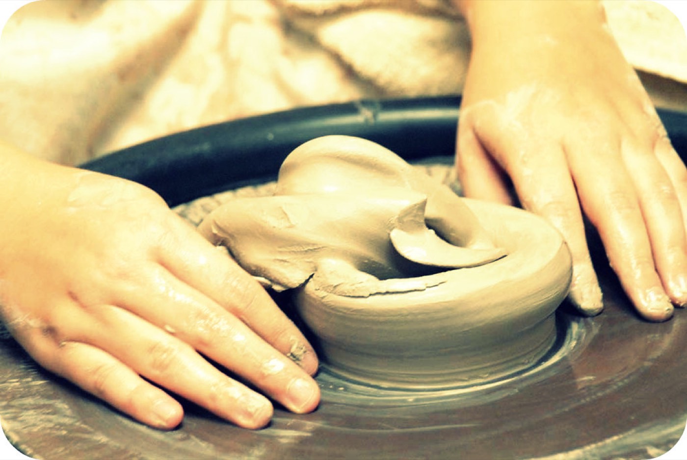 Hands shaping wet clay on a potter's wheel
