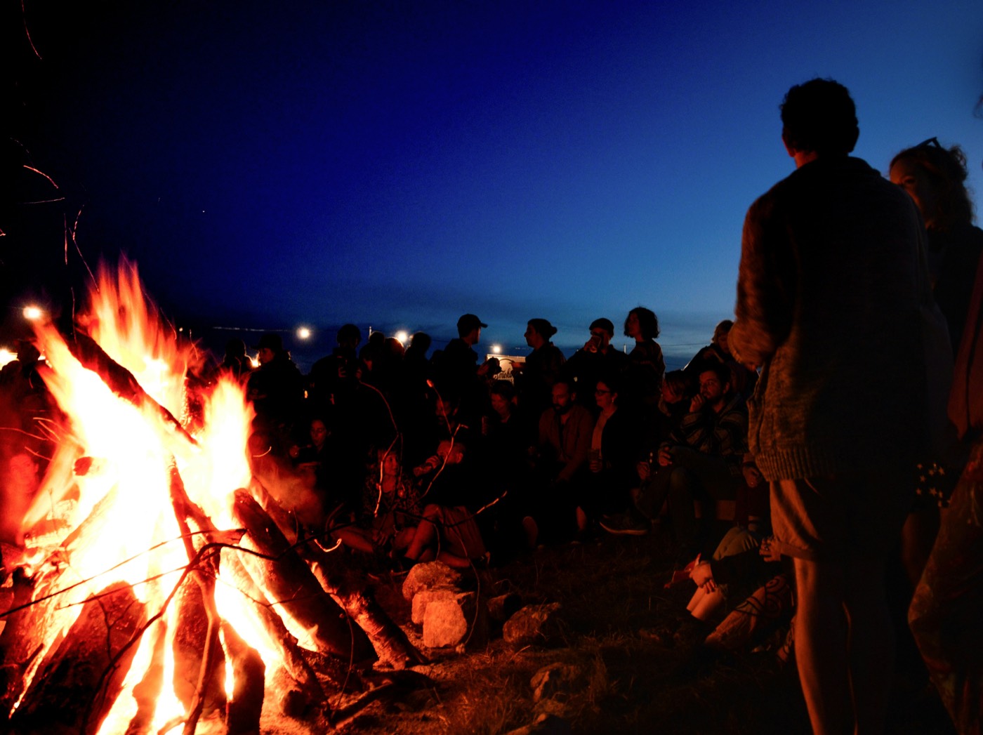 A crowd gathered around a bonfire at dusk